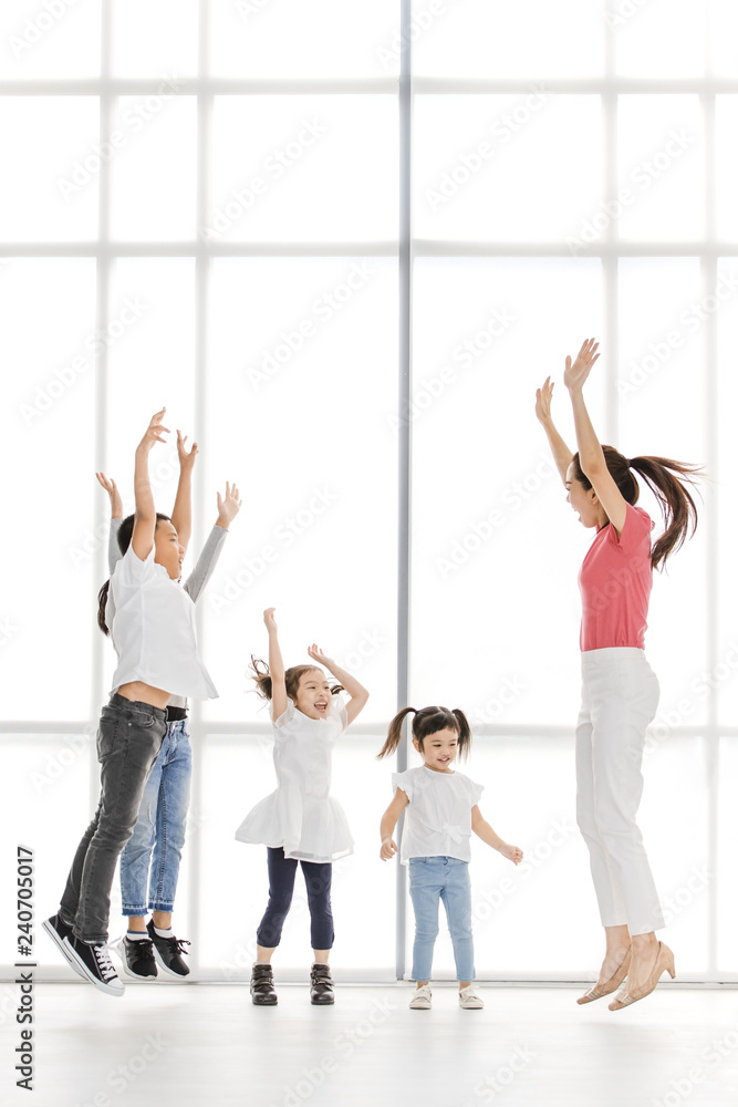 Obraz premium Asian woman in pink shirt playing something with Asian boy ans girls, they jump together, they stand in front of big white window.