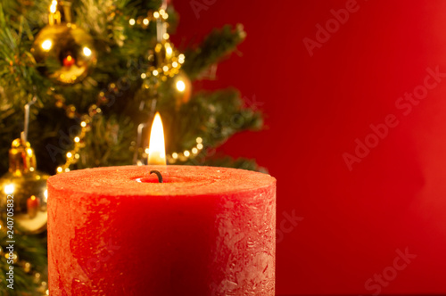 Greeting card with lighted candle with the blurred Xmas tree on red background