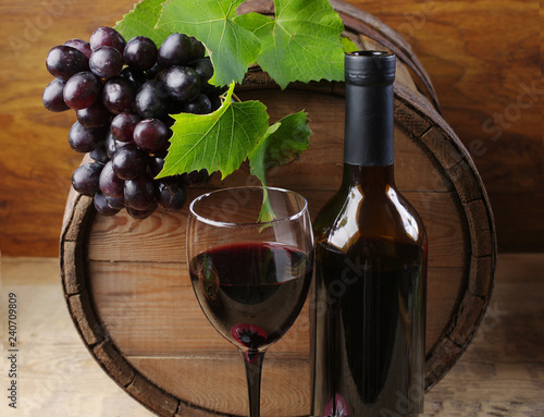 BottA bottle of wine and a glass of wine  a grape on the background of a wine barrel.