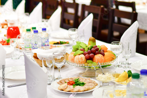 details of serving tables for a banquet in a restaurant. grapes  kiwi  tangerines  deli meats  white plates and white napkins. wine glass and vodka glasses on the table. selective focus