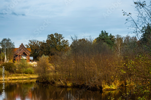 The sky, the forest, the house under construction are reflected in the still water of the lake in autumn.
