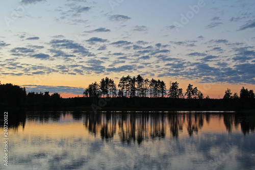 Fototapeta Naklejka Na Ścianę i Meble -  Silhouettes of trees and colorful sky are reflected in the forest lake in the evening. Unusual and picturesque scene. Russia.