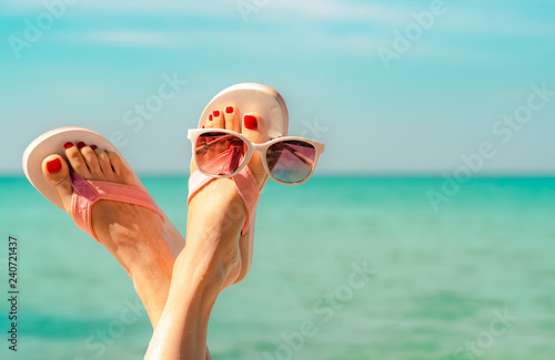 Upside woman feet and red pedicure wearing pink sandals, sunglasses at seaside. Funny and happy fashion young woman relax on vacation. Chill out girl at beach. Creative for tour agent. Weekend travel.