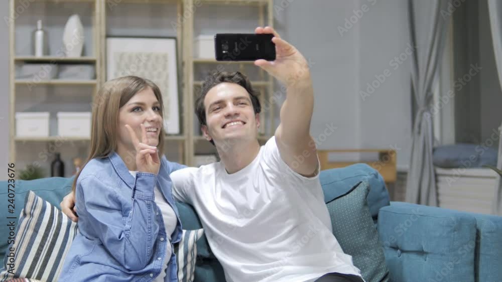 Young Couple Taking Selfie with Smartphone while Sitting on Couch Young Couple Taking Selfie with Smartphone while Sitting on Couch