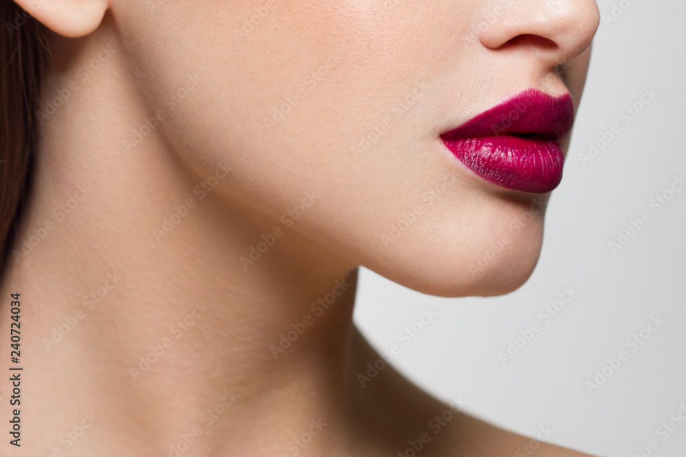 Fototapeta premium Kosmetyki, makijaż i trendy. Jasny błyszczyk i szminka na ustach. Zbliżenie piękne kobiece usta z różowym makijażem warg. Piękna część kobiecej twarzy. Idealnie czysta skóra w różowym świetle