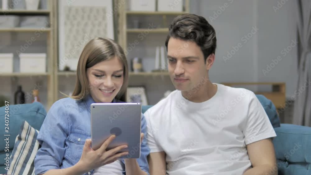 Young Couple Browsing Internet on Tablet while Relaxing on Couch Young Couple Browsing Internet on Tablet while Relaxing on Couch