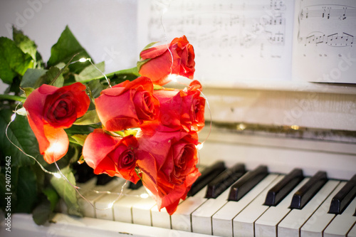 Red roses on a white piano with notes and garlands