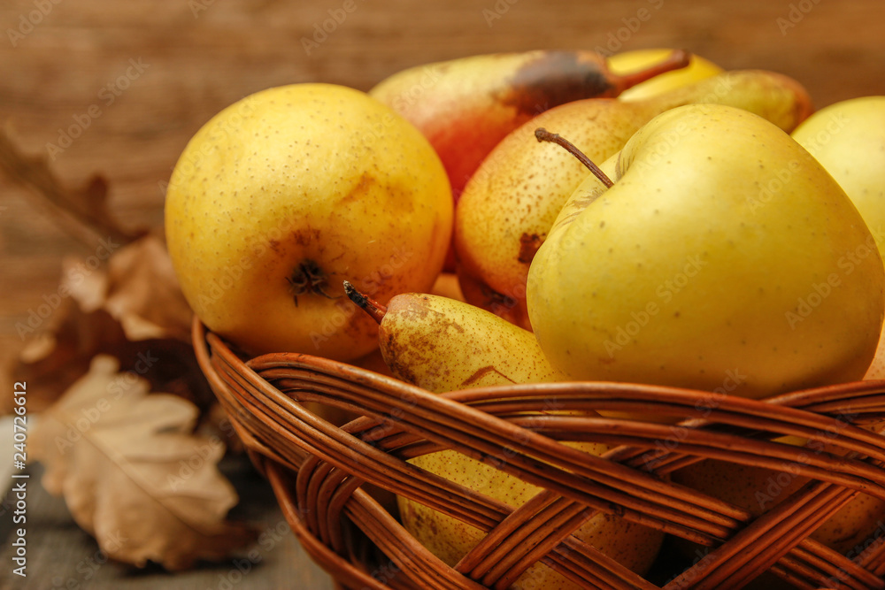 Fresh raw organic pears and apples in a basket on rustic wooden table. Close-up.