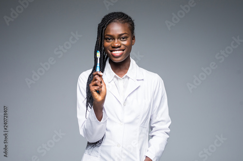Beautiful african female dentist doctor holding and showing a toothbrush isolated on a gray background