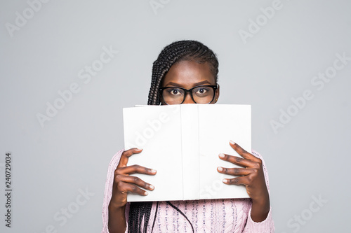 Portrait of a young woman hiding behind a book with glasses, isolated on a gray background © F8  \ Suport Ukraine
