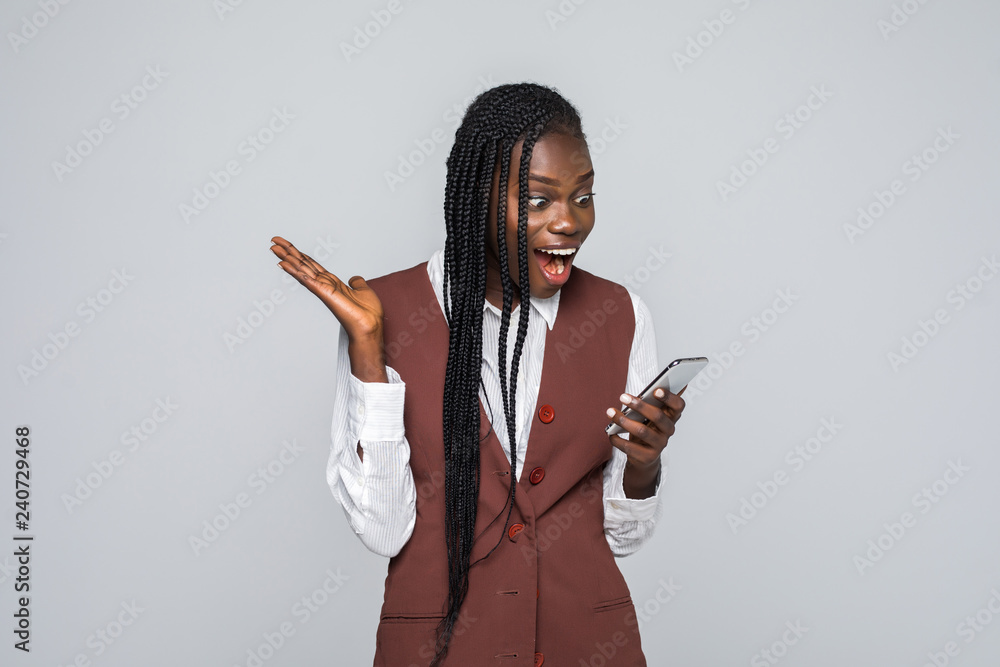 Portrait of shocked young african woman holding mobile phone over gray background