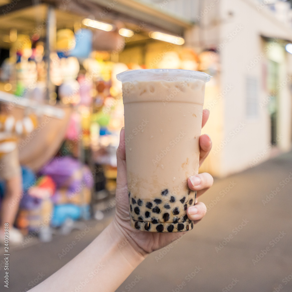A young woman is holding a plastic cup of brown sugar bubble milk tea at a night market in Taiwan, Taiwan delicacy, close up. A young woman is holding a plastic cup of brown sugar bubble milk tea at a night market in Taiwan, Taiwan delicacy, close up.