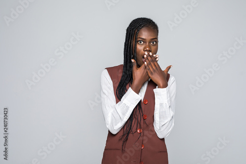 Shocked young african woman covering her mouth and looking at the camera over gray background