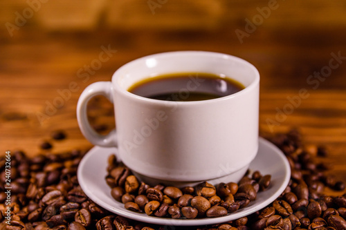 Cup of hot coffee and scattered coffee beans on wooden table