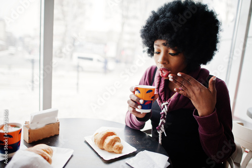 Curly hair african american woman wear on sweater posed at cafe indoor with cup of tea or coffee.