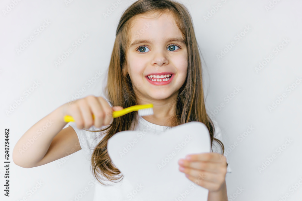 Little cute baby girl with toothbrush and tooth layout in hand. The concept of health, oral hygiene, people and beauty. The layout of the space. Selective focus. Little cute baby girl with toothbrush and tooth layout in hand. The concept of health, oral hygiene, people and beauty. The layout of the space. Selective focus.