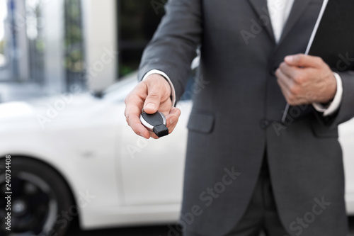 Car salesman holding key and presenting new auto