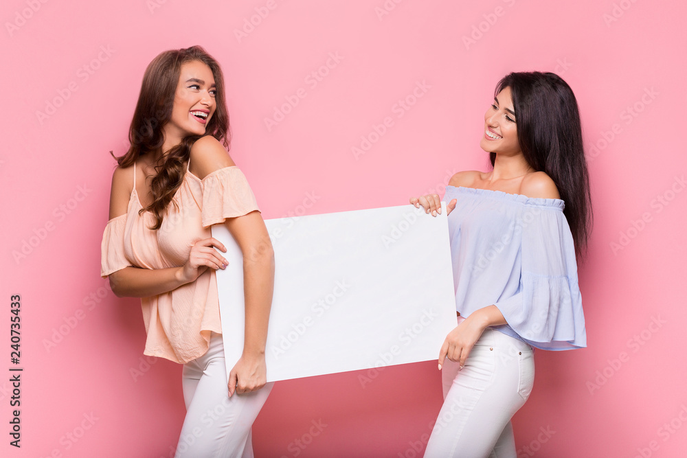 Happy girl friends holding blank advertisement board Happy girl friends holding blank advertisement board