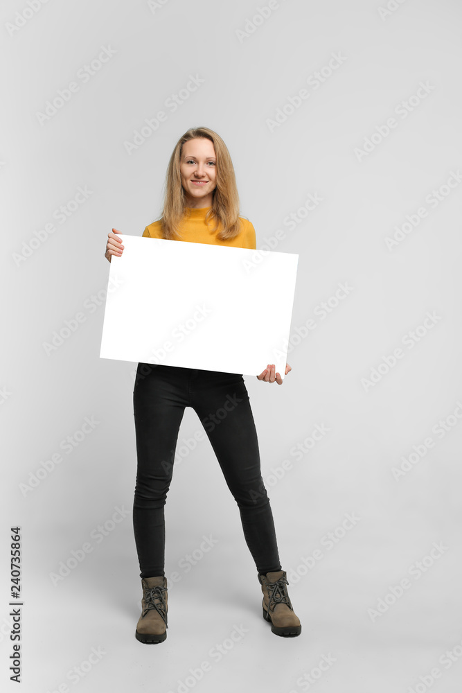 Close up portrait of positive laughing woman wearing black jeans and yellow t-shirt with blondie hair, toothy smile is holding white big mockup poster isolated on white background Close up portrait of positive laughing woman wearing black jeans and yellow t-shirt with blondie hair, toothy smile is holding white big mockup poster isolated on white background