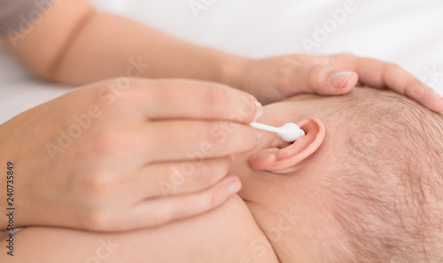 Mother hand cleaning baby ear with cotton swab