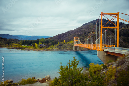 Red suspension bridge over the water runoff of General Carrera Lake, near Lake Bertrand, Puerto Tranquilo, Chile Chico, Aysen, Chile, Patagonia photo