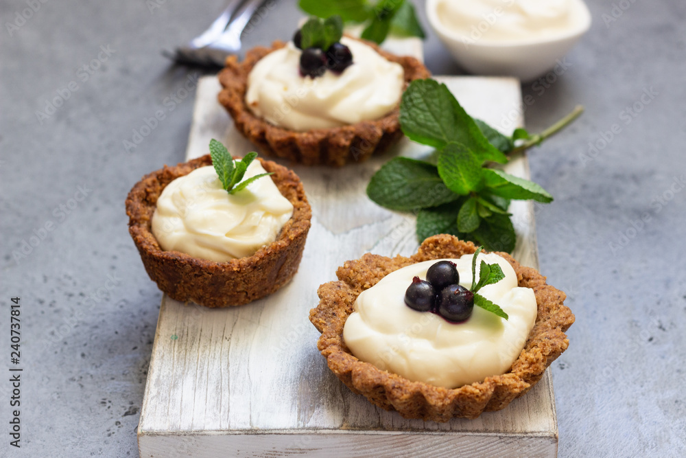 Mini tarts (tartlets) with whipped cream or custard and fresh berries served with mint. Homemade dessert. Grey background. Copy space. Mini tarts (tartlets) with whipped cream or custard and fresh berries served with mint. Homemade dessert. Grey background. Copy space.