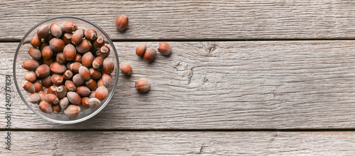 Bowl with unpeeled hazelnuts on wooden background