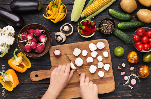 Female hand cutting fresh radishes on board