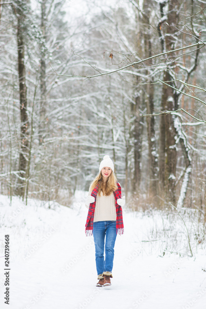 Young happy woman in winter clothes walks in the snowy forest