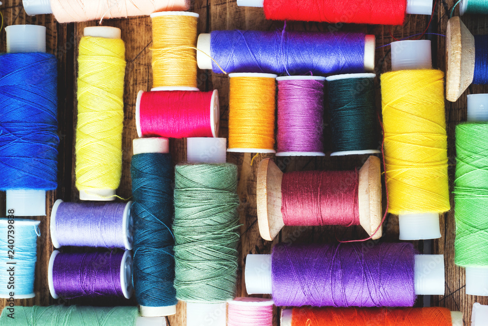Colored spools of thread laid out in rows on wooden background.