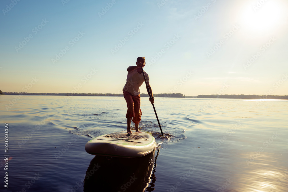 Joyful guy paddling on a SUP board