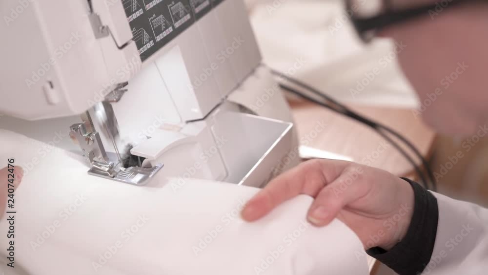 A close-up top view of a seamstress stitching white fabric on the sewing machine. The process of sewing a wedding dress A close-up top view of a seamstress stitching white fabric on the sewing machine. The process of sewing a wedding dress
