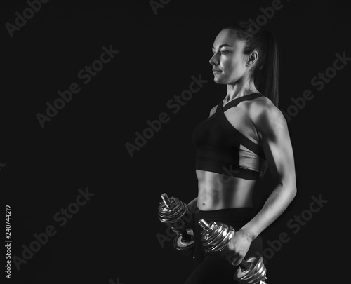 Woman bodybuilder with dumbbells at black background