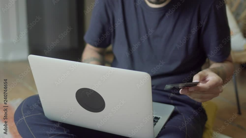 Tattooed man with credit card using laptop. Cropped shot of young man holding credit card and using laptop at home. Online shopping concept Tattooed man with credit card using laptop. Cropped shot of young man holding credit card and using laptop at home. Online shopping concept