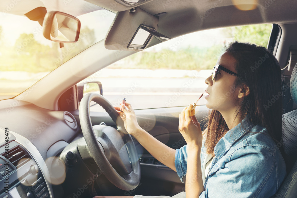 Naklejka premium woman looking in rear view mirror and making up in car
