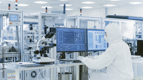 In Laboratory Over the Shoulder View of Scientist in Protective Clothes Doing Research on a Personal Computer. Modern Manufactory Producing Semiconductors and Pharmaceutical Items. photo