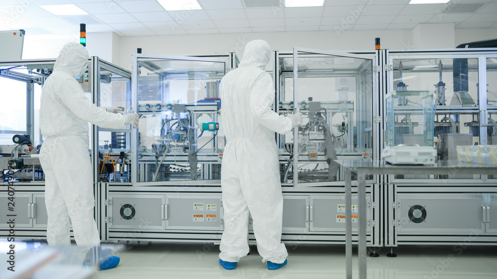 Naklejka premium In the Manufacturing Facility Team of Scientist Wearing Sterile Protective Coverall Set's up / Programs Modern Industrial 3D Printer, High Precision Manufacture of Semiconductors under Process.