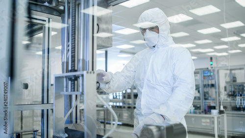 In Manufacturing Facility Shot of Scientist in Sterile Protective Clothing Work on a Modern Industrial 3D Printing Machinery. Pharmaceutical, Biotechnological Manufacturing Process. Shot from Inside.