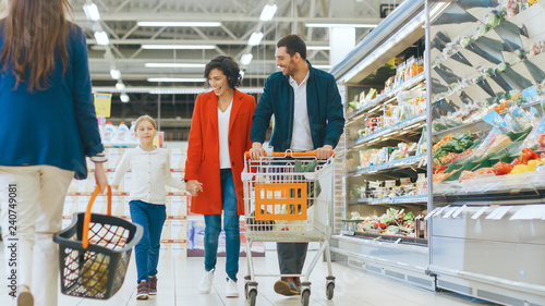 At the Supermarket: Happy Family of Three, Holding Hands, Walks Through Fresh Produce Section of the Store. Father, Mother and Daughter Having Fun Time Shopping. photo