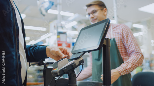 Foto At the Supermarket: Checkout Counter Customer Pays with Smartphone for His Food Items
