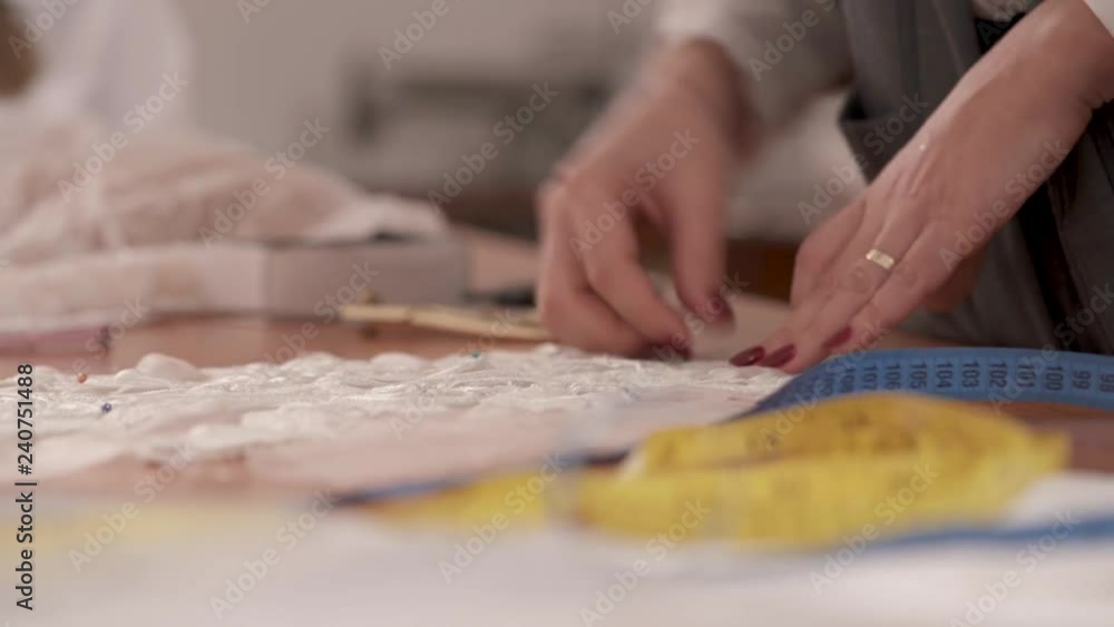 A closeup of woman's manicure hands taking pins out of cutout pieces of fabric for the wedding dress. A closeup of woman's manicure hands taking pins out of cutout pieces of fabric for the wedding dress.