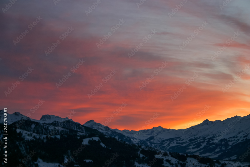 shades of orange and pink clouds explode over the snow-capped Alps in this epic mountain sunset