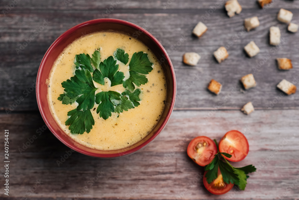Pumpkin cream soup in bowl with parsley on wooden table with crackers and tomatoes. Traditional autumn food for Halloween Pumpkin cream soup in bowl with parsley on wooden table with crackers and tomatoes. Traditional autumn food for Halloween
