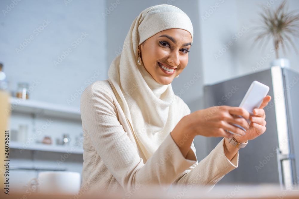 young muslim woman using smartphone and smiling at camera young muslim woman using smartphone and smiling at camera