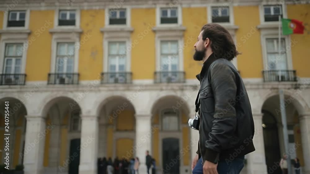 Smiling bearded man with photo camera walking against old yellow building. Smiling bearded man with photo camera walking against old yellow building.