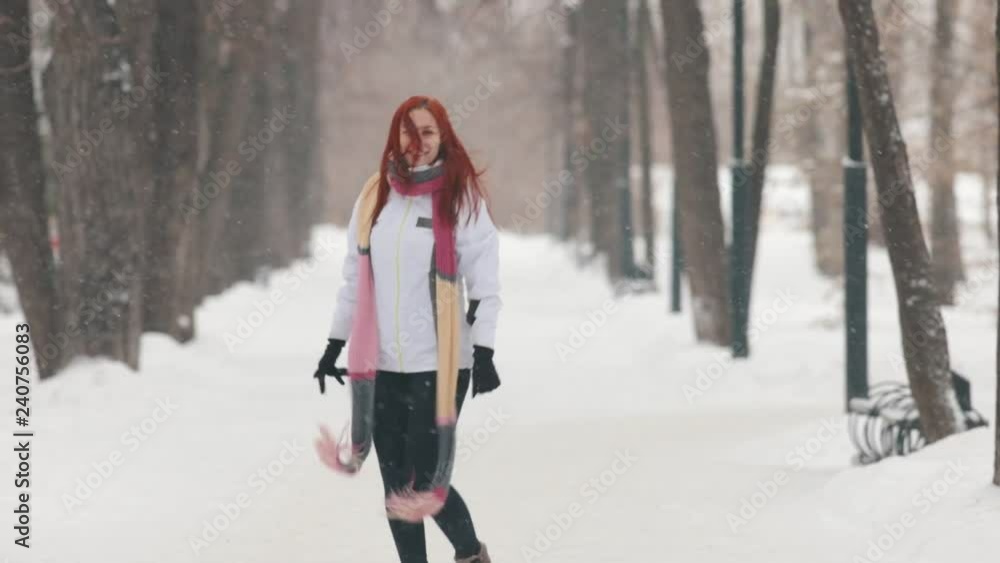 Winter park. A woman with bright red hair standing on the sidewalk. Jumping and waving her hand Winter park. A woman with bright red hair standing on the sidewalk. Jumping and waving her hand