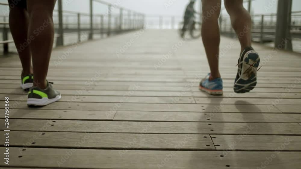 Close up shot of sportsmen legs in sneakers walking on wooden pier. Rear view of two african american men strolling. Sport concept Close up shot of sportsmen legs in sneakers walking on wooden pier. Rear view of two african american men strolling. Sport concept