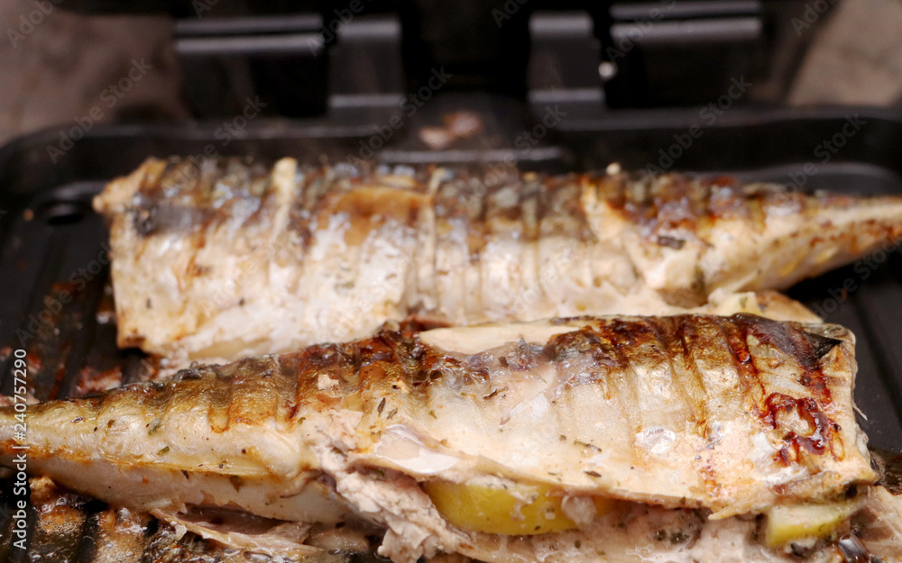 Mackerel is roasted on an electric grill. Grilled fish with lemon and salad