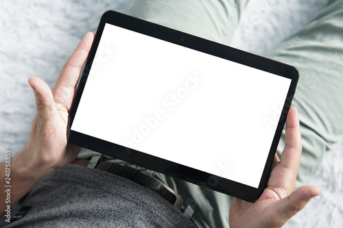 Top-down shot of digital tablet in young man's hands sititng comfortably on a sofa. Close up of man's hands holding tablet with an blank white screen. Holding the tablet without touching the screen photo