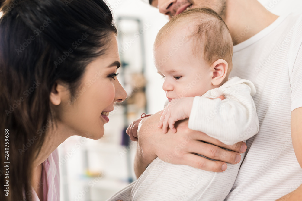 smiling mother looking at little son on fathers hands at home smiling mother looking at little son on fathers hands at home